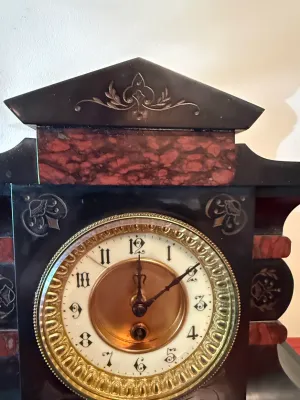 Sale Photo Thumbnail #123: Antique French mantle clock with black and faux-red marble finish, featuring incised floral details and an ornate brass bezel around a white dial with Arabic numerals.