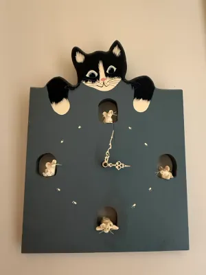 Sale Photo Thumbnail #424: Whimsical folk art wooden wall clock featuring a painted black-and-white cat peering over the top, mouse figures in cutouts at the cardinal hours, and painted paw print hour markers.