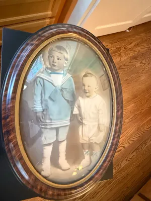 Sale Photo Thumbnail #342: Antique oval-framed portrait of two young children, featuring hand-tinted details and convex bubble glass in a dark wood and gilt frame.