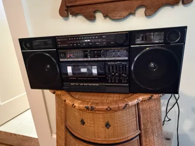 Sale Photo Thumbnail #347: Vintage Fisher stereo cassette boombox with detachable speakers, featuring an equalizer and radio tuner, sitting atop a woven rattan chest.