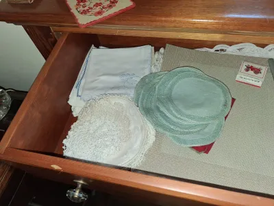 Sale Photo Thumbnail #112: Wooden dresser drawer filled with assorted vintage linens, including embroidered handkerchiefs, crocheted doilies, fabric coasters, and place mats.