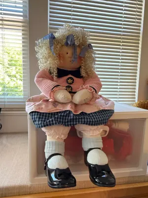 Sale Photo Thumbnail #357: Handmade soft sculpture doll with curly yarn hair, blue ribbons, a pink outfit, and black patent shoes.