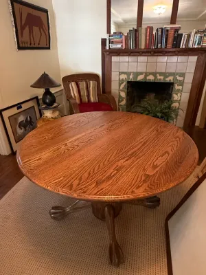 Sale Photo Thumbnail #167: Round oak pedestal dining table with claw feet, set in a living area beside a fireplace with decorative tile surround.