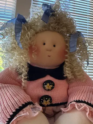 Sale Photo Thumbnail #356: Handmade cloth doll featuring blonde curly yarn hair tied with blue ribbons and a pink knit sweater with floral buttons.
