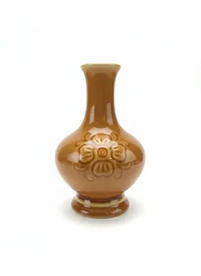 Sale Photo Thumbnail #70: Glossy ochre glazed ceramic vase featuring an embossed floral emblem and a flared pedestal base.