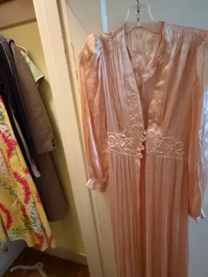 Sale Photo Thumbnail #337: Vintage light pink satin robe with embroidered floral detail and long sleeves, hanging on a plastic hanger.