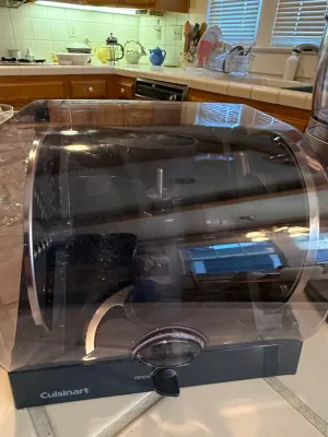 Sale Photo Thumbnail #438: Cuisinart food processor accessory holder with clear plastic domed lid and dark base, housing various blades and discs.