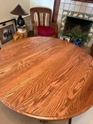 Sale Photo Thumbnail #164: Round oak dining table with prominent wood grain, set in a living room near a fireplace and armchair.