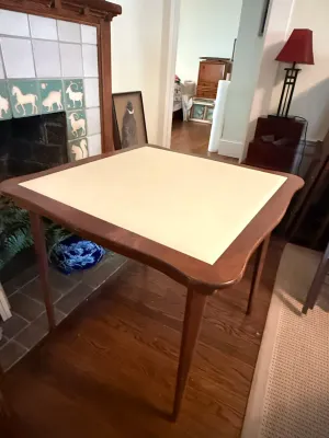 Sale Photo Thumbnail #241: Mid-century wooden folding card table featuring a light-colored vinyl inlaid top surface and tapered legs.