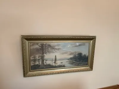 Sale Photo Thumbnail #239: Framed horizontal landscape painting depicting a sailboat on a lake, housed in an ornate molded gold frame.