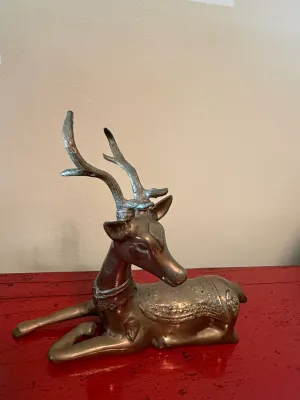 Sale Photo Thumbnail #158: Vintage brass reclining deer figurine with ornate embossed saddle details and textured antlers, resting on a red surface.