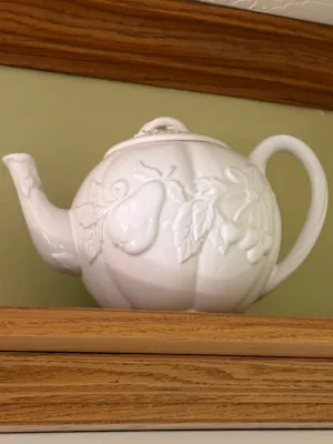 Sale Photo Thumbnail #449: White ceramic teapot featuring embossed fruit and leaf motifs, including pears and cherries, with a matching lid.