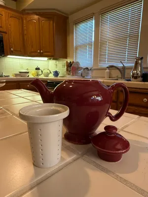 Sale Photo Thumbnail #467: Burgundy ceramic teapot with a removable lid and a white ceramic loose-leaf tea infuser insert.
