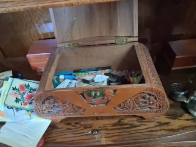 Sale Photo Thumbnail #60: Hand-carved wooden trinket box with a hinged lid, filled with various pens, cards, and small desktop items.