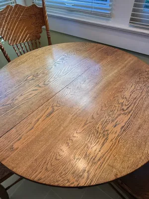 Sale Photo Thumbnail #414: Round oak dining table with prominent wood grain, paired with a matching carved press-back chair.