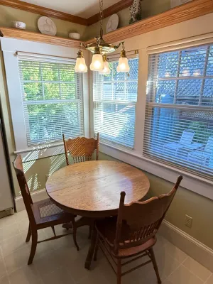 Sale Photo Thumbnail #413: Round wooden breakfast table paired with three mismatched wooden chairs in a bright dining nook, illuminated by a brass four-light chandelier.