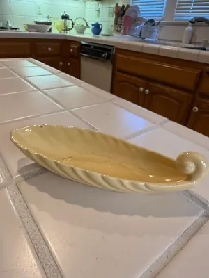 Sale Photo Thumbnail #490: Vintage pale yellow glazed ceramic boat-shaped console bowl featuring fluted sides and a scrolled tail handle.