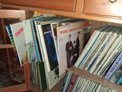 Sale Photo Thumbnail #161: Collection of vintage vinyl LP records stacked in a wooden cabinet, featuring a copy of 'Introducing... The Beatles' on Vee-Jay Records.