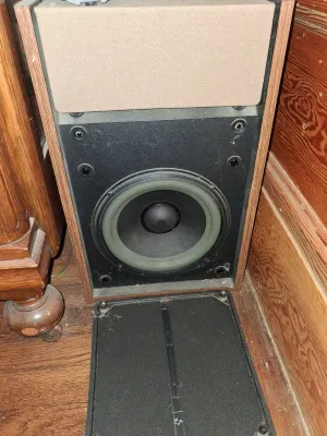 Sale Photo Thumbnail #90: Vintage wood veneer speaker cabinet with a beige cloth upper section and a exposed woofer, showing signs of dust and age.