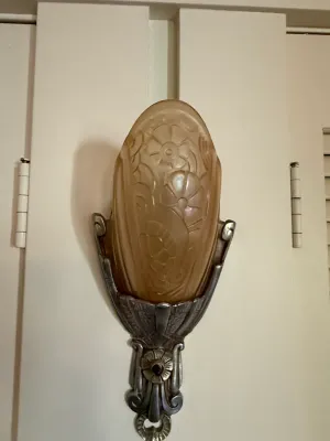 Sale Photo Thumbnail #415: Art Deco wall sconce featuring a frosted amber glass shade with floral reliefs mounted in an ornate silver-tone metal frame.