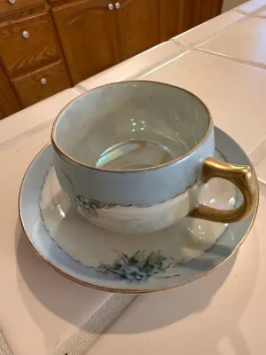 Sale Photo Thumbnail #454: Vintage iridescent porcelain teacup and saucer set featuring hand-painted blue floral details and gilt accents.