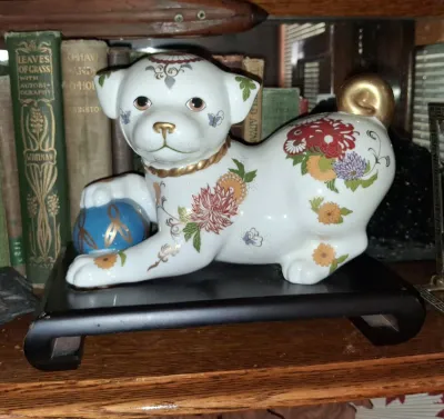 Sale Photo Thumbnail #38: Japanese Kutani porcelain puppy figurine hand-painted with colorful floral motifs and gold accents, resting on a black wooden display stand.