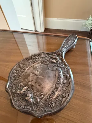 Sale Photo Thumbnail #248: Vintage Art Nouveau silver-plated hand mirror featuring ornate embossed floral and scrollwork detailing.