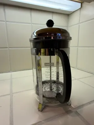 Sale Photo Thumbnail #481: Bodum French press coffee maker with a stainless steel frame, glass beaker, and black plastic handle.