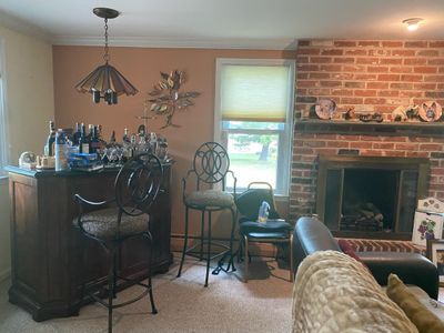 Home bar set with a wooden cabinet counter, metal swivel barstools with patterned upholstered seats, and hanging stained glass light...