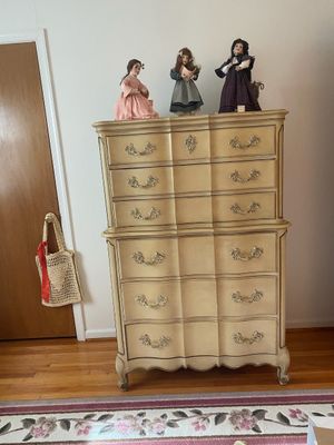 French Provincial style chest-on-chest in a cream finish with brass hardware, featuring three collectible porcelain dolls displayed on top.