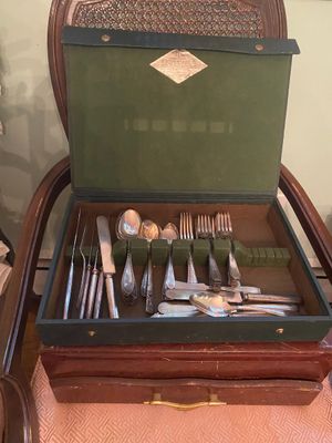 Vintage silver-plated flatware set housed in a green felt-lined presentation case, displayed on a wooden armchair.