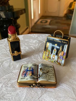 Trio of hand-painted porcelain Limoges trinket boxes, including a medical textbook with miniature stethoscope, a lipstick tube, and a...