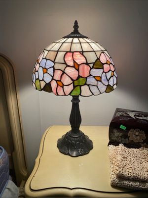 Tiffany-style stained glass table lamp featuring a floral shade with pink and blue blossoms on a dark cast metal base.