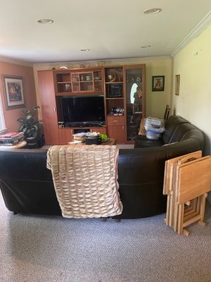 Living room setup featuring a dark brown leather sectional sofa, a large wooden entertainment center with flat-screen television, and a...