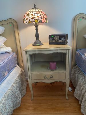 French Provincial style nightstand flanked by matching twin beds, featuring a Tiffany-style stained glass lamp and a mother-of-pearl...