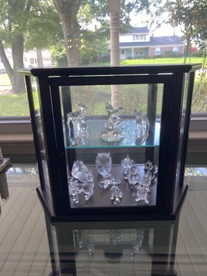 Dark wood hexagonal display cabinet with glass panels, containing a collection of miniature crystal animal figurines including an owl,...