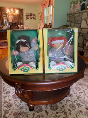 Pair of vintage 1985 Cabbage Patch Kids dolls in original display boxes, featuring one dark-haired doll and one red-haired doll in gray...