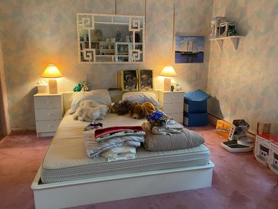 Bedroom suite featuring a white platform bed frame, matching three-drawer nightstands, lamps, and a white Faux Bamboo Greek key wall mirror.
