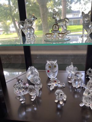 Collection of faceted crystal animal figurines displayed in a glass display cabinet, including Swarovski style deer, owls, and a tea set.