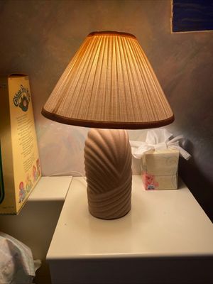 Vintage 1980s textured ceramic table lamp with a pleated beige lampshade, shown illuminated on a nightstand.