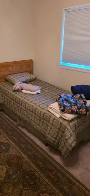 Sale Photo Thumbnail #44: Twin bed with a light oak headboard, geometric patterned bedspread, and folded linens atop, set alongside an patterned area rug.
