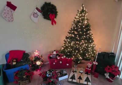 Sale Photo Thumbnail #67: Assorted Christmas holiday decorations featuring a pre-lit artificial Christmas tree, hanging stockings, pine wreath, storage totes with garland, and faux poinsettias.