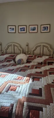 Sale Photo Thumbnail #49: A pair of twin beds pushed together featuring cream-painted arched headboards with dark accent trim, topped with a large log cabin pattern patchwork quilt.