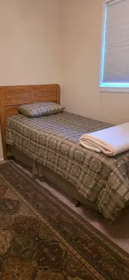 Sale Photo Thumbnail #64: Twin-sized oak headboard bed frame with patterned bedding and a matching pillow, presented alongside an ornate area rug.