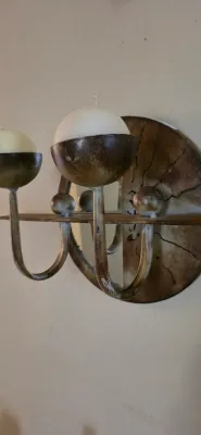Sale Photo Thumbnail #5: Rustic metal wall sconce featuring a round mirrored backplate, sunburst detailing, and curved arms holding spherical candle cups with white candles.