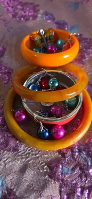 Sale Photo Thumbnail #13: Collection of vibrant costume jewelry, featuring yellow and orange plastic bangle bracelets paired with metallic and faux pearl dangle earrings.