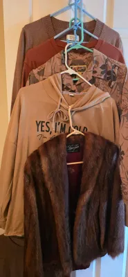 Sale Photo Thumbnail #40: Collection of men's and women's tops layered on plastic hangers, including a vintage Lauer Furs brown fur jacket, a tan hooded sweatshirt, a floral button-up shirt, and knit sweaters.