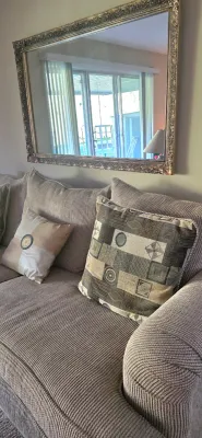 Sale Photo Thumbnail #8: Contemporary ribbed fabric sofa styled with accent pillows and a large ornate silver-framed wall mirror hanging above.