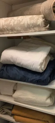 Sale Photo Thumbnail #30: Linen closet filled with stacked blankets, comforters, a floral jacquard bedspread, and a dark blue oversized hoodie blanket.