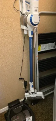 Sale Photo Thumbnail #29: Wall-mounted Tineco cordless stick vacuum cleaner with charger, displayed next to a folded step ladder and a Samsung robot vacuum base.